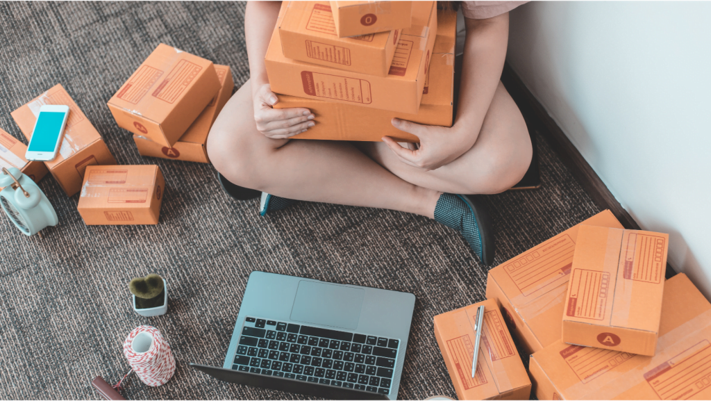 caja de envíos en una alfombra, un laptop y la piernas de una mujer sosteniendo en sus piernas cajas de envío social selling