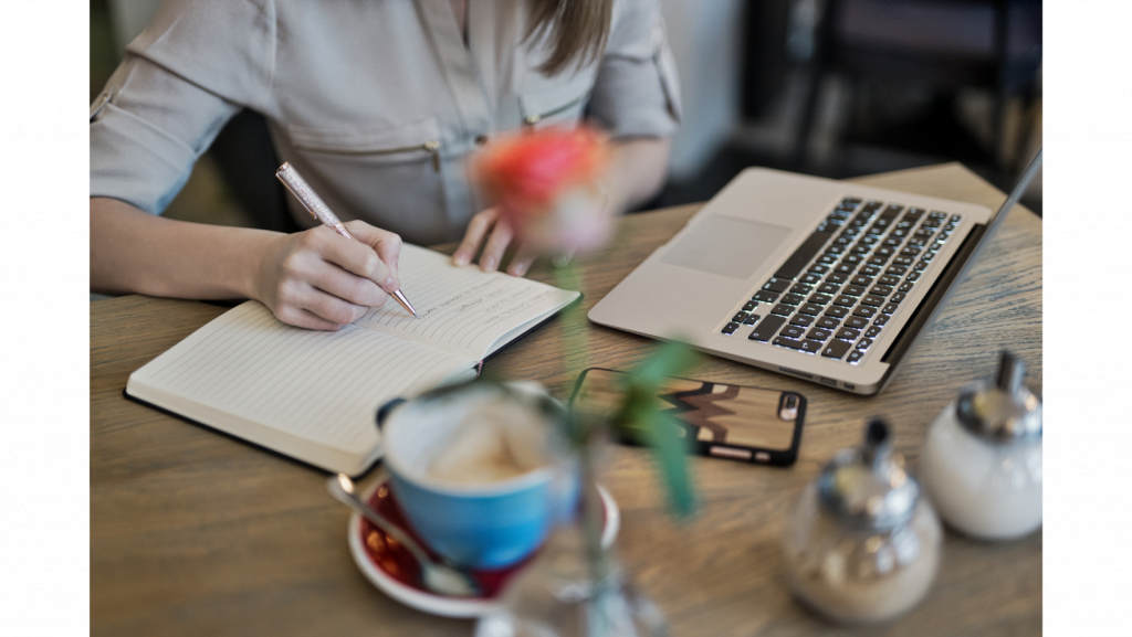 escritorio de trabajo con laptop, móvil, manos de mujer escribiendo, taza de café y otros elementos estrategias de Whatsapp Multiagente 
